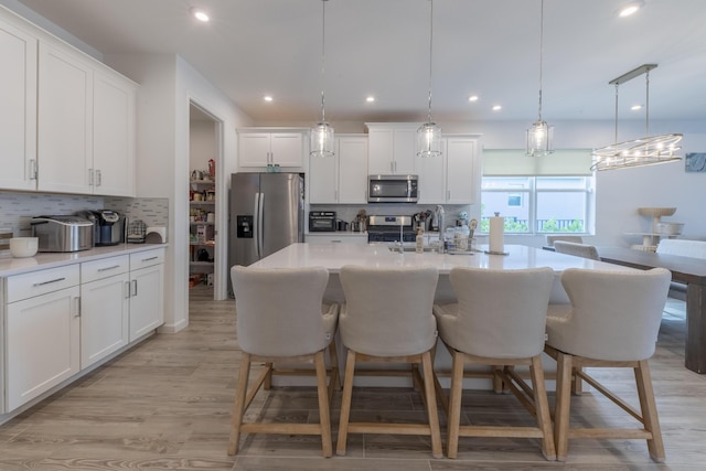 kitchen with white cabinetry, an island with sink, stainless steel appliances, decorative light fixtures, and sink