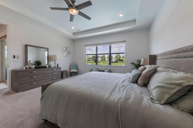 carpeted bedroom with ceiling fan and a tray ceiling