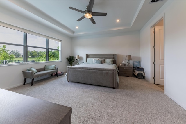 bedroom with ceiling fan, light colored carpet, and a tray ceiling