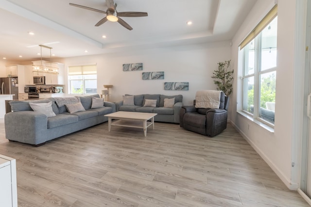 living room with ceiling fan, a raised ceiling, a wealth of natural light, and light hardwood / wood-style flooring