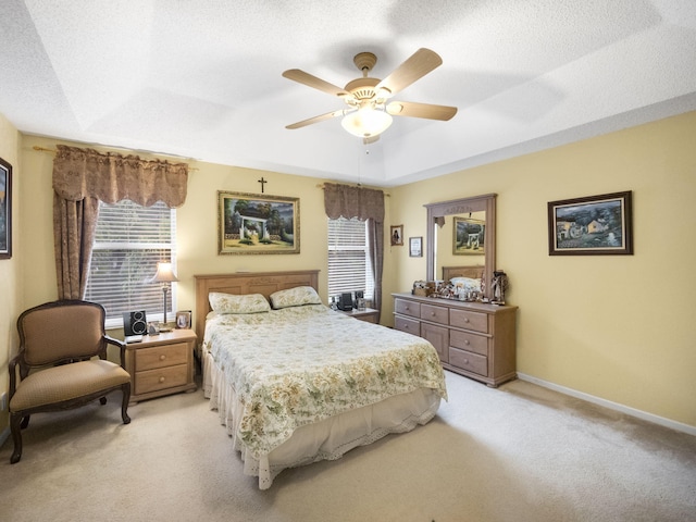 bedroom with a textured ceiling, ceiling fan, light colored carpet, and a tray ceiling