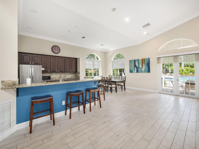 kitchen featuring a kitchen bar, tasteful backsplash, ornamental molding, stainless steel refrigerator, and dark brown cabinets