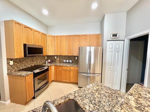 kitchen featuring tasteful backsplash, light tile patterned floors, stainless steel appliances, and dark stone countertops