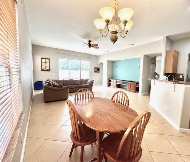 tiled dining space featuring ceiling fan with notable chandelier and sink