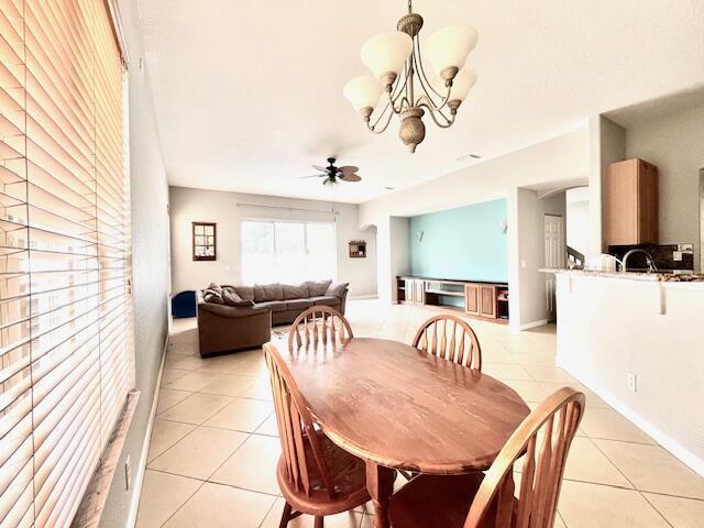 tiled dining room with ceiling fan with notable chandelier