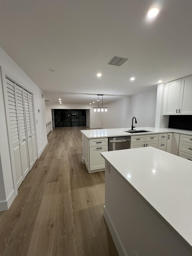 kitchen with decorative light fixtures, light hardwood / wood-style floors, stainless steel dishwasher, sink, and white cabinets