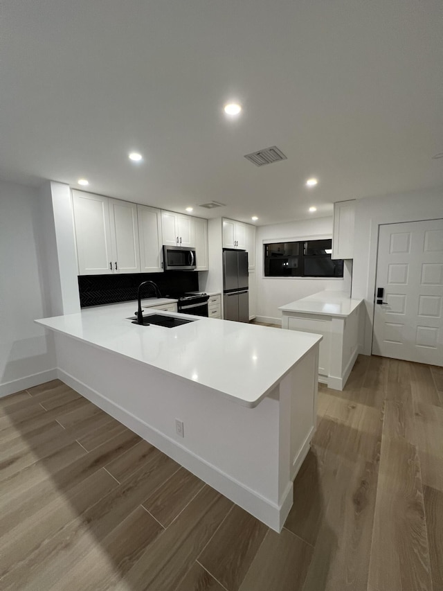 kitchen with kitchen peninsula, appliances with stainless steel finishes, white cabinets, light hardwood / wood-style flooring, and sink