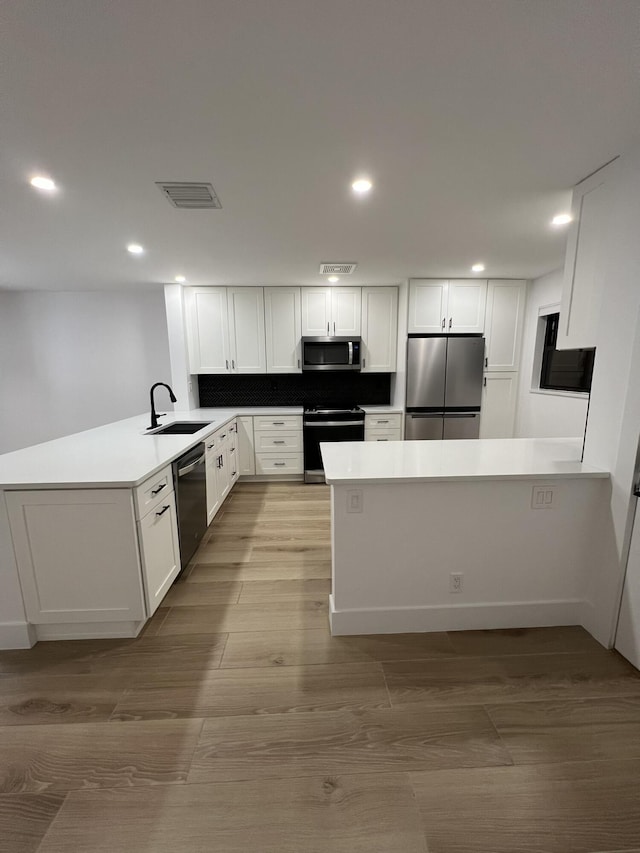 kitchen with white cabinets, appliances with stainless steel finishes, sink, kitchen peninsula, and light hardwood / wood-style flooring