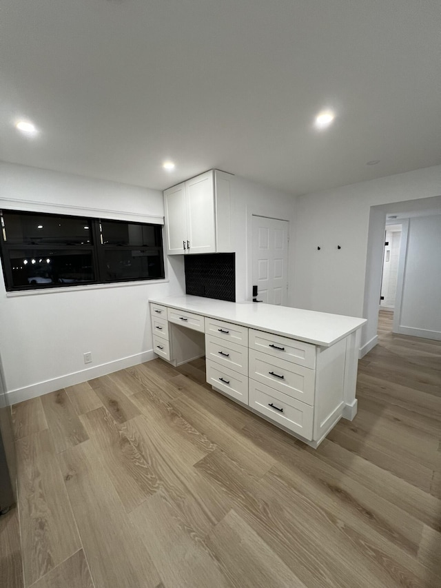 kitchen with white cabinetry, built in desk, light hardwood / wood-style flooring, and kitchen peninsula