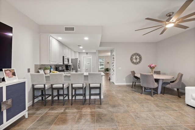 kitchen with a breakfast bar, white cabinetry, backsplash, stainless steel appliances, and kitchen peninsula