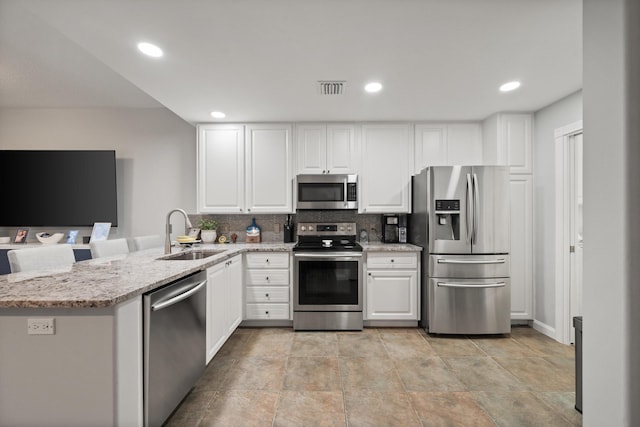 kitchen with sink, white cabinetry, light stone counters, kitchen peninsula, and stainless steel appliances