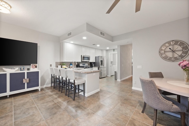 kitchen with sink, a breakfast bar area, white cabinets, stainless steel appliances, and light stone countertops