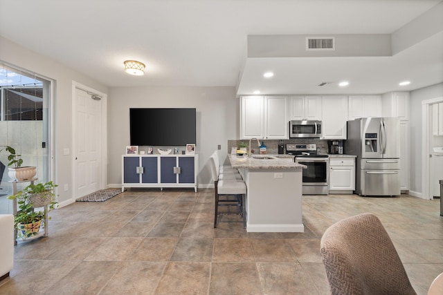 kitchen with white cabinets, a kitchen breakfast bar, kitchen peninsula, stainless steel appliances, and light stone countertops