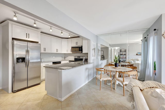 kitchen featuring dark stone countertops, kitchen peninsula, white cabinetry, stainless steel appliances, and light tile patterned floors