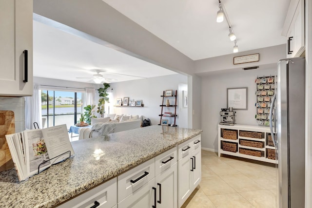 kitchen with ceiling fan, light stone countertops, white cabinetry, and stainless steel refrigerator