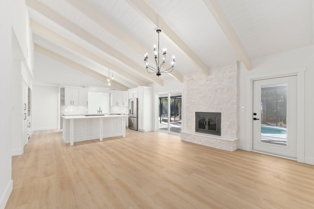 unfurnished living room featuring lofted ceiling with beams, sink, light hardwood / wood-style flooring, a stone fireplace, and a chandelier