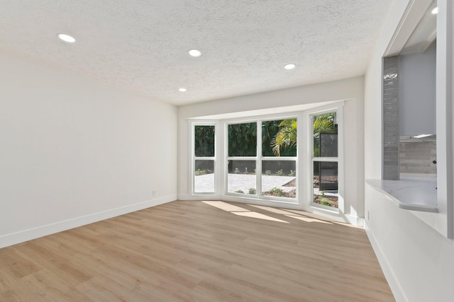 spare room with a textured ceiling and light hardwood / wood-style floors