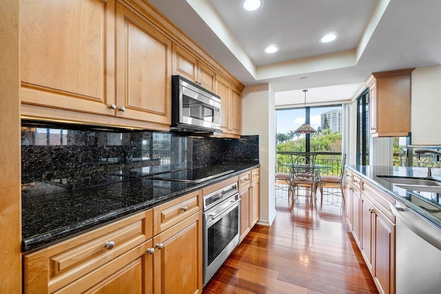 kitchen featuring decorative light fixtures, dark stone countertops, a raised ceiling, stainless steel appliances, and dark hardwood / wood-style flooring