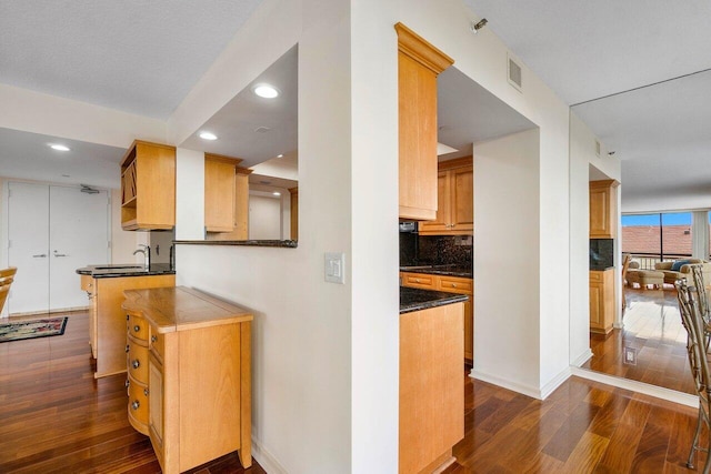 kitchen featuring decorative backsplash, dark hardwood / wood-style floors, kitchen peninsula, and dark stone countertops