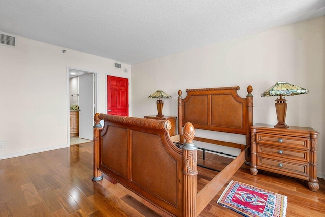 bedroom featuring a textured ceiling, connected bathroom, and hardwood / wood-style flooring