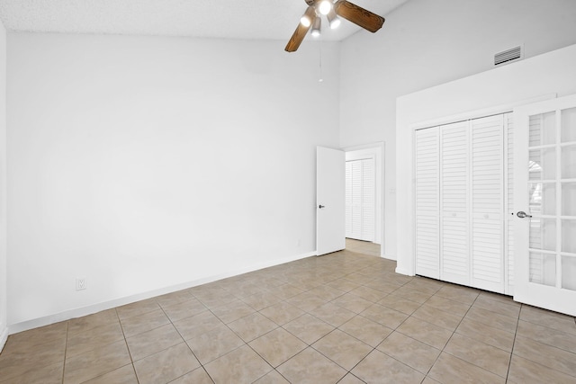 unfurnished bedroom with a towering ceiling, light tile patterned floors, ceiling fan, a textured ceiling, and a closet