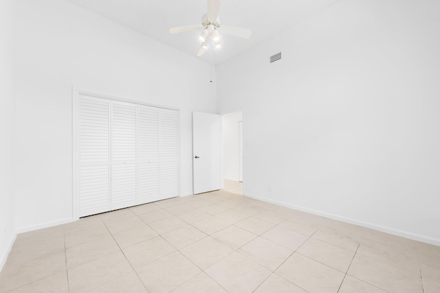 unfurnished bedroom featuring ceiling fan, a towering ceiling, a closet, and light tile patterned floors