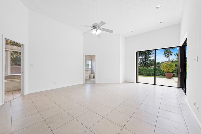 empty room featuring a towering ceiling, light tile patterned floors, a textured ceiling, and ceiling fan