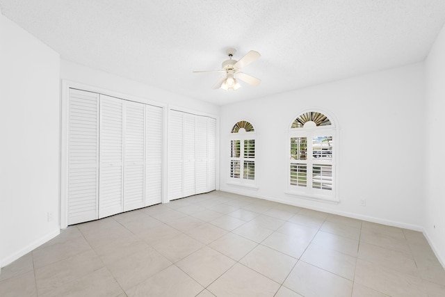 unfurnished bedroom with two closets, a textured ceiling, ceiling fan, and light tile patterned floors