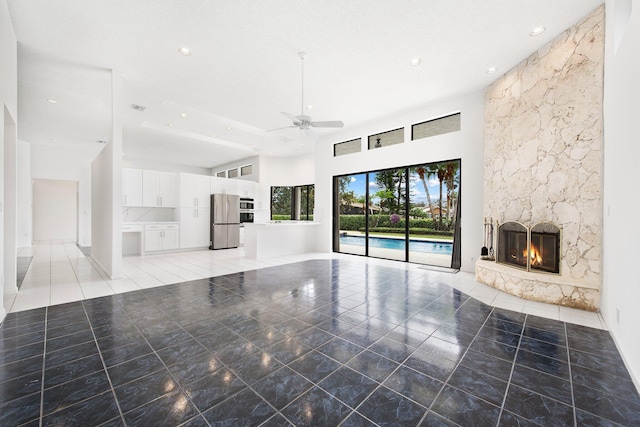 unfurnished living room featuring a high ceiling, ceiling fan, and a fireplace