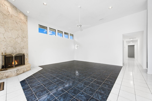 interior space with ceiling fan, a stone fireplace, tile patterned flooring, and a towering ceiling