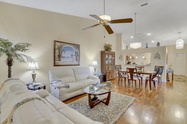 living room with ceiling fan with notable chandelier, lofted ceiling, and light hardwood / wood-style floors