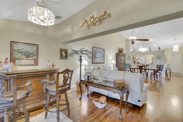 living room with high vaulted ceiling, bar area, ceiling fan with notable chandelier, and hardwood / wood-style flooring