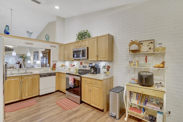 kitchen with stainless steel appliances, high vaulted ceiling, light wood-type flooring, light stone countertops, and sink