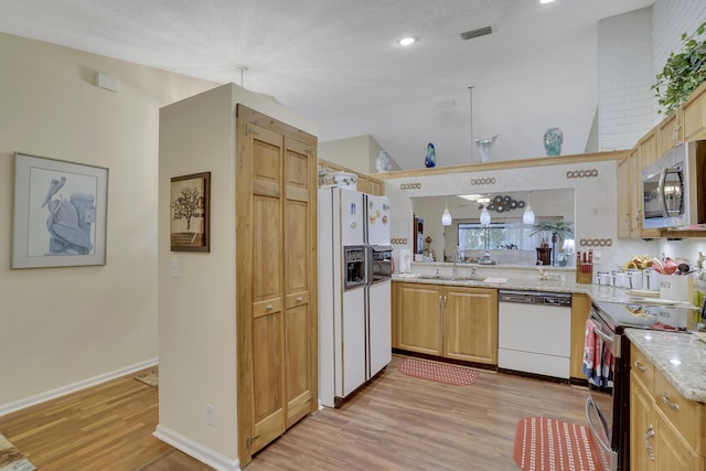 kitchen with light stone countertops, appliances with stainless steel finishes, sink, kitchen peninsula, and light hardwood / wood-style flooring