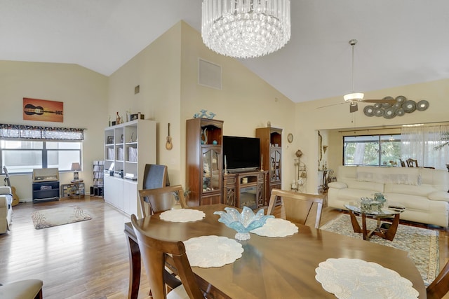 dining area with ceiling fan with notable chandelier, wood-type flooring, and high vaulted ceiling