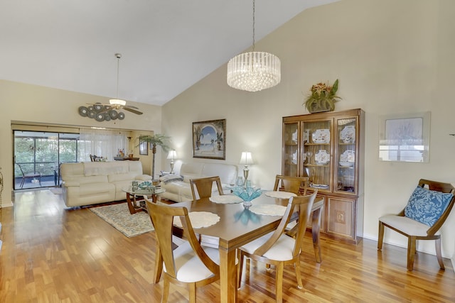 dining space with high vaulted ceiling, light wood-type flooring, and ceiling fan with notable chandelier