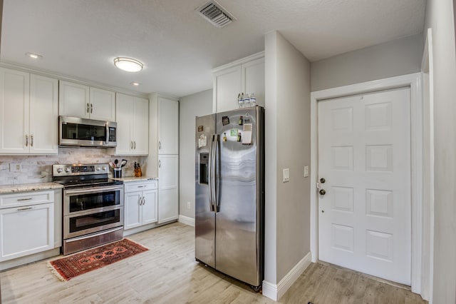 kitchen featuring stainless steel appliances, white cabinets, and backsplash