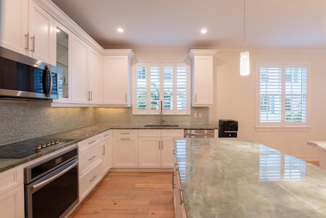 kitchen featuring appliances with stainless steel finishes, decorative light fixtures, white cabinetry, sink, and light stone counters