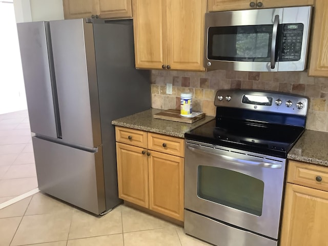 kitchen featuring stainless steel appliances, light tile patterned floors, decorative backsplash, and dark stone countertops