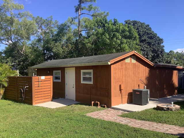 view of outdoor structure featuring an outdoor fire pit, a yard, and central air condition unit