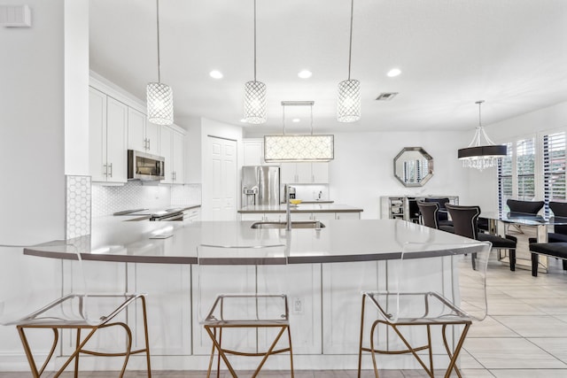 kitchen featuring white cabinetry, stainless steel appliances, decorative light fixtures, and a kitchen breakfast bar