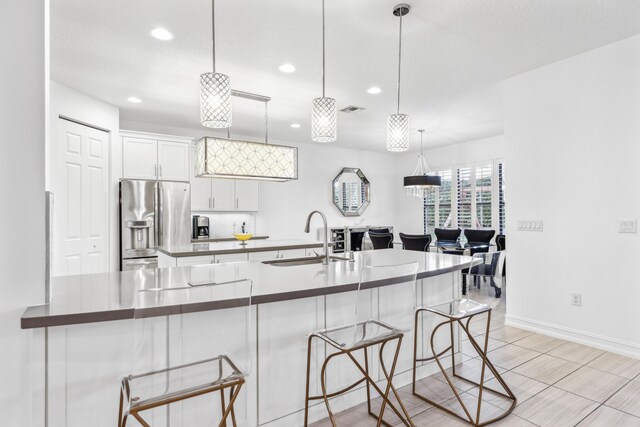 kitchen with white cabinetry, stainless steel appliances, decorative light fixtures, a kitchen island, and sink