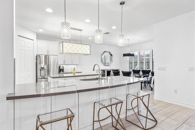 kitchen with a breakfast bar, decorative light fixtures, sink, white cabinets, and stainless steel refrigerator with ice dispenser