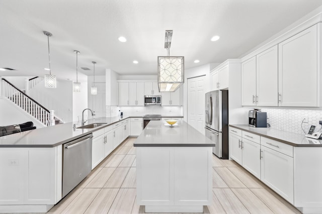 kitchen featuring appliances with stainless steel finishes, pendant lighting, white cabinetry, sink, and a center island