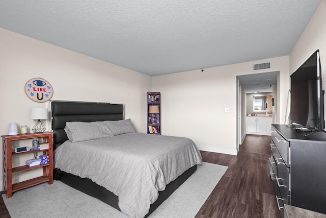 bedroom with ensuite bathroom, dark hardwood / wood-style floors, and a textured ceiling