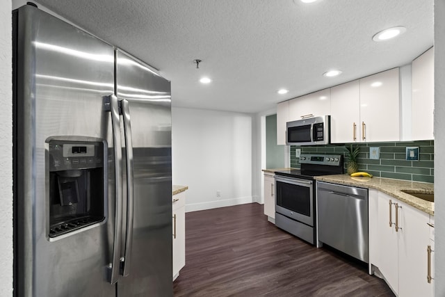 kitchen with light stone countertops, appliances with stainless steel finishes, white cabinetry, dark hardwood / wood-style flooring, and tasteful backsplash