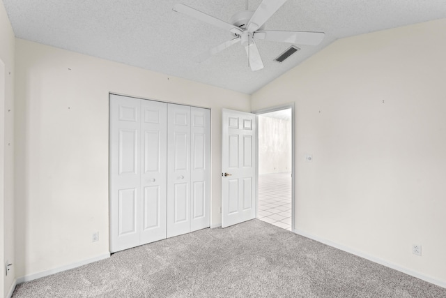 unfurnished bedroom with lofted ceiling, light colored carpet, ceiling fan, a textured ceiling, and a closet