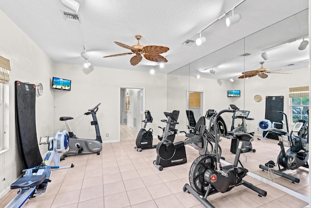 gym with ceiling fan, light tile patterned flooring, track lighting, and a textured ceiling