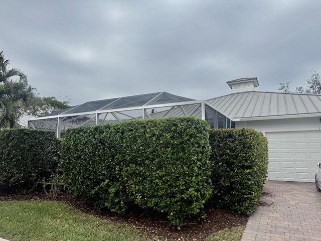 3289 Wymberly Dr, Jupiter, FL 33458 - view of side of property featuring a standing seam roof, a garage, glass enclosure, and a metal roof