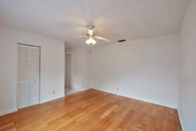 unfurnished bedroom featuring ceiling fan, two closets, a textured ceiling, and light wood-type flooring